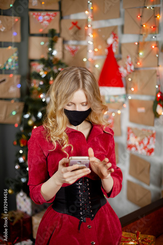 Portrait of a beautiful girl in medical mask, standing in front of decorated christmas tree at home