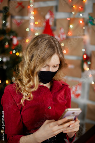 Portrait of a beautiful girl in medical mask, standing in front of decorated christmas tree at home