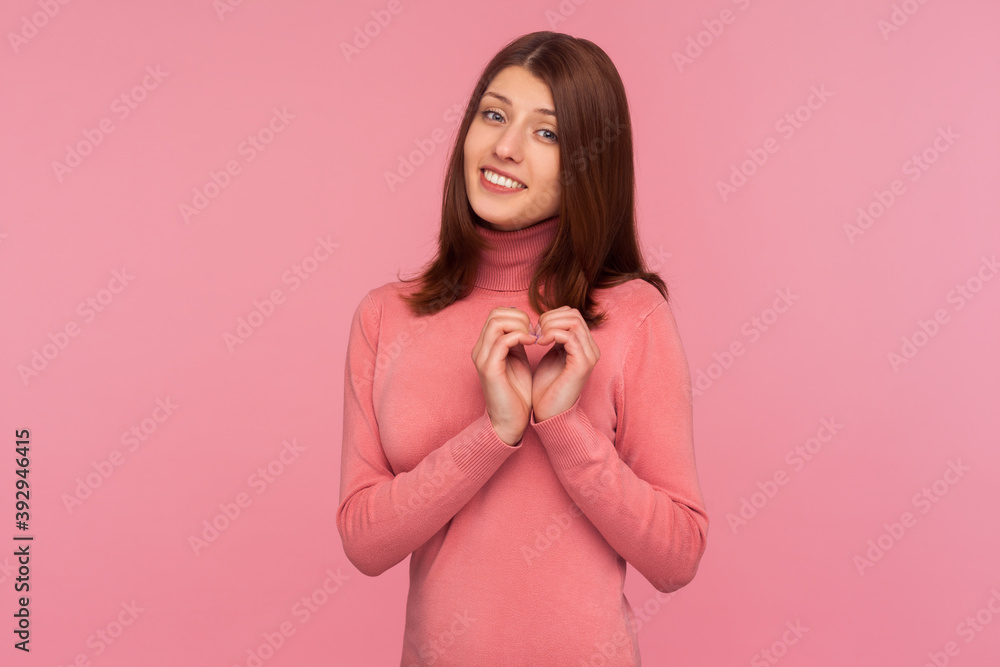 Cute pretty brunette woman in pink sweater showing heart gesture with hands near her chest, symbol of love and charity. Indoor studio shot isolated on pink background Cute pretty brunette woman in pink sweater showing heart gesture with hands near her chest, symbol of love and charity. Indoor studio shot isolated on pink background