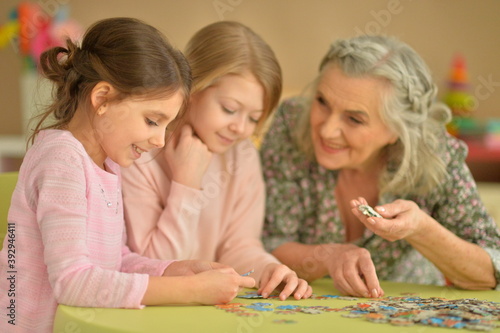 Portrait of grandmother with little granddaughters collecting puzzle