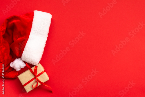 Santa Claus hat and gift box on light red background. Christmas and New Year concept. © Inna