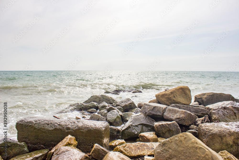 Stormy sea. Powerful large foam waves beat against rocks and rocks. A scattering of spray. Cloudy weather with bright light. Stormy sea. Powerful large foam waves beat against rocks and rocks. A scattering of spray. Cloudy weather with bright light.