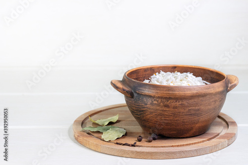 Homemade sauerkraut in a wooden bowl. Dish is decorated with a bay leaf and peppercorns.