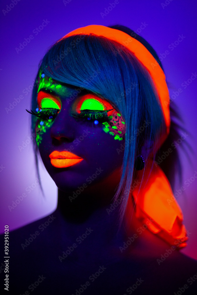 Close up UV front portrait of a girl with artistic colorful makeup and orange scarf, isolated violet blue background.