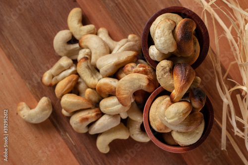 cashew nuts on a wooden table and in two wooden cups with straw background.