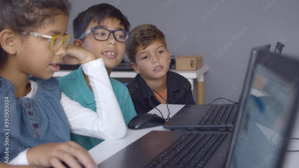 Schoolchildren doing task together, helping each other, using laptops ...