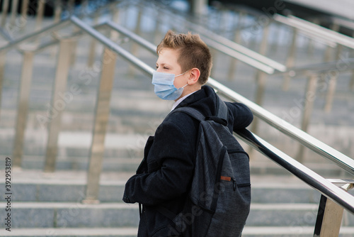 Schoolboy walks out of school wearing protective mask in a city