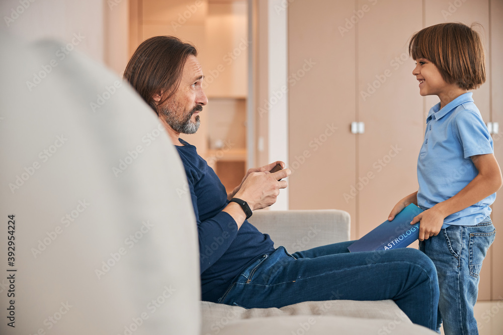 Obraz premium Cheerful child bringing a book for his father to read