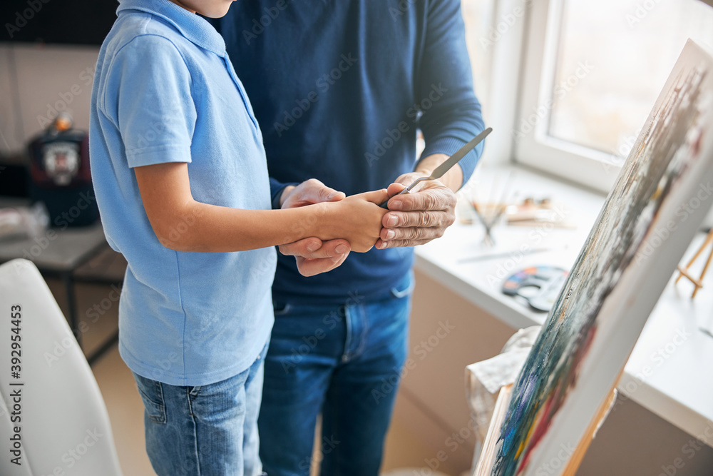 Knowledgeable father teaching a boy to paint with palette-knife