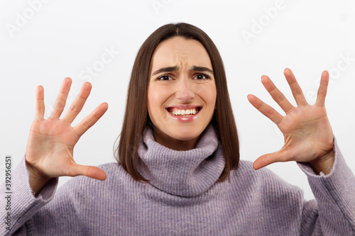 Clueless satisfied young female has spreads hands with hesitation, can not make choice between two nice products, feels doubtful, wears red loose clothes, isolated over white background.