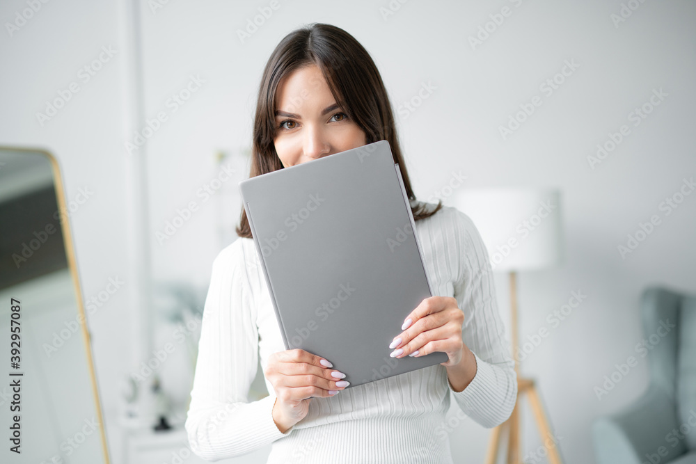 .Young woman stands and covers her face with laptop. .Young woman stands and covers her face with laptop.