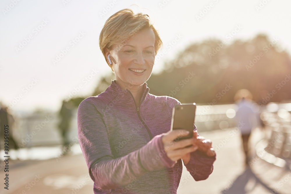Results speak for themselves. Portrait of joyful active mature woman in sportswear using her smartphone, checking result after running outdoors on a sunny day Results speak for themselves. Portrait of joyful active mature woman in sportswear using her smartphone, checking result after running outdoors on a sunny day