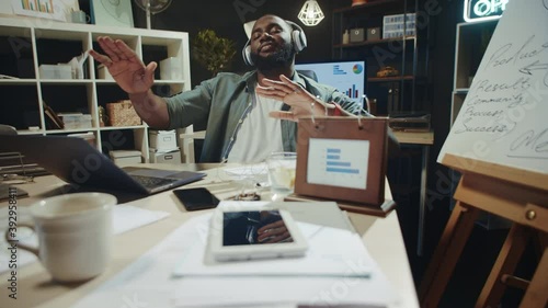 Relaxed afro manager chilling in headphones near laptop at modern workplace