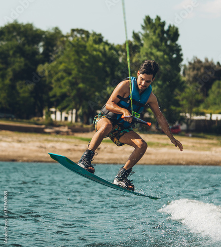 young man doing wakeboarding in a lake whit mountains also doing jumps