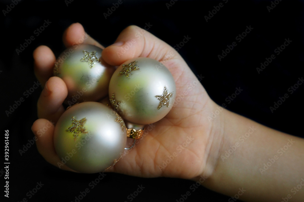 three white Christmas toys round with silver stars lie in a child's small hand on a black background top view. symbols of Christmas and New Year holidays three white Christmas toys round with silver stars lie in a child's small hand on a black background top view. symbols of Christmas and New Year holidays