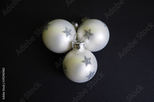 three white Christmas toys round with silver stars lie on a black background side view . symbols of Christmas and new year holidays