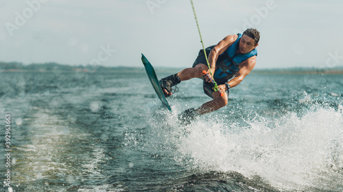 young man doing wakeboarding in a lake whit mountains also doing jumps