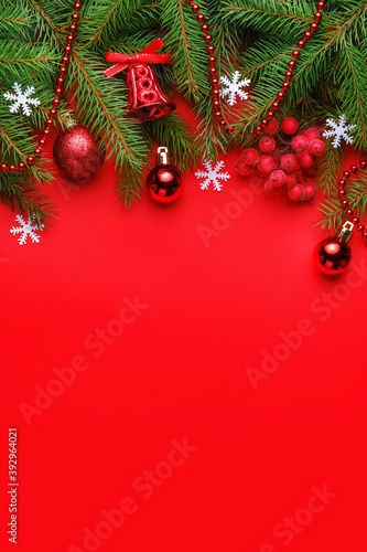 Top view of Christmas composition with spruce branches  snowflakes  balls  red berries and bell on red background. Christmas background concept  vertical orientation  copy space