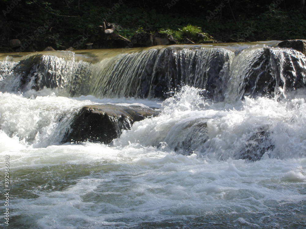 Stone cascade with a waterfall on a mountain river with streams of white water with foam and splashes Stone cascade with a waterfall on a mountain river with streams of white water with foam and splashes