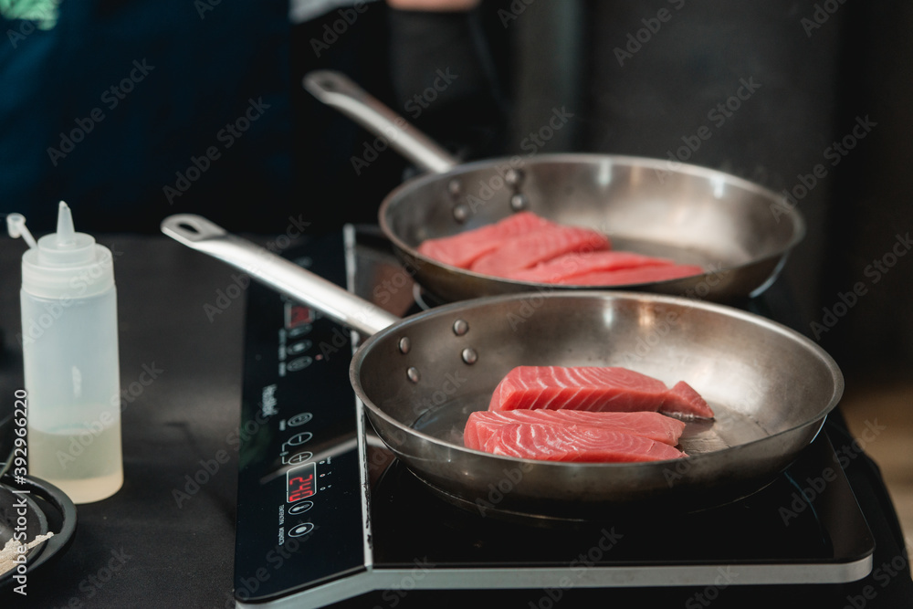 Two frying pans with tuna steak on induction stove Two frying pans with tuna steak on induction stove