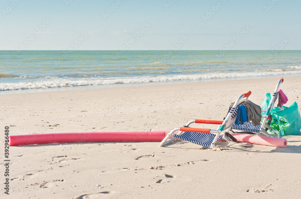 from view, medium distance of two colorful, empty beach chairs with towels and beach bag, floatation device in the tropical sand on a beach on gulf of Mexico on sunny morning from view, medium distance of two colorful, empty beach chairs with towels and beach bag, floatation device in the tropical sand on a beach on gulf of Mexico on sunny morning
