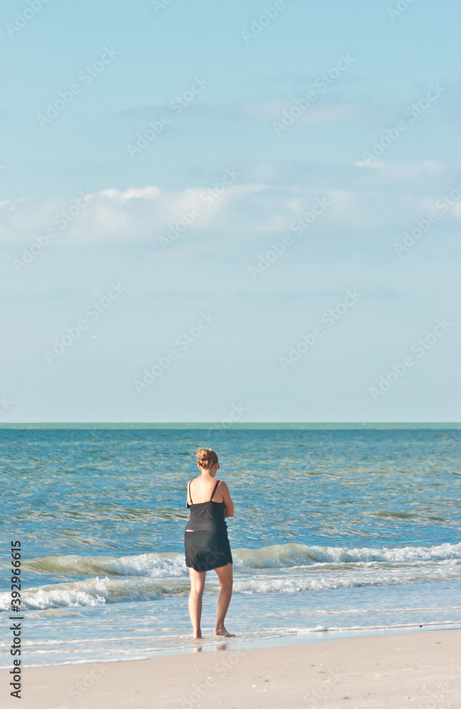 back view, far distance of a middle aged female walking along a tropical, sandy beach on gulf of Mexico. on a sunny morning