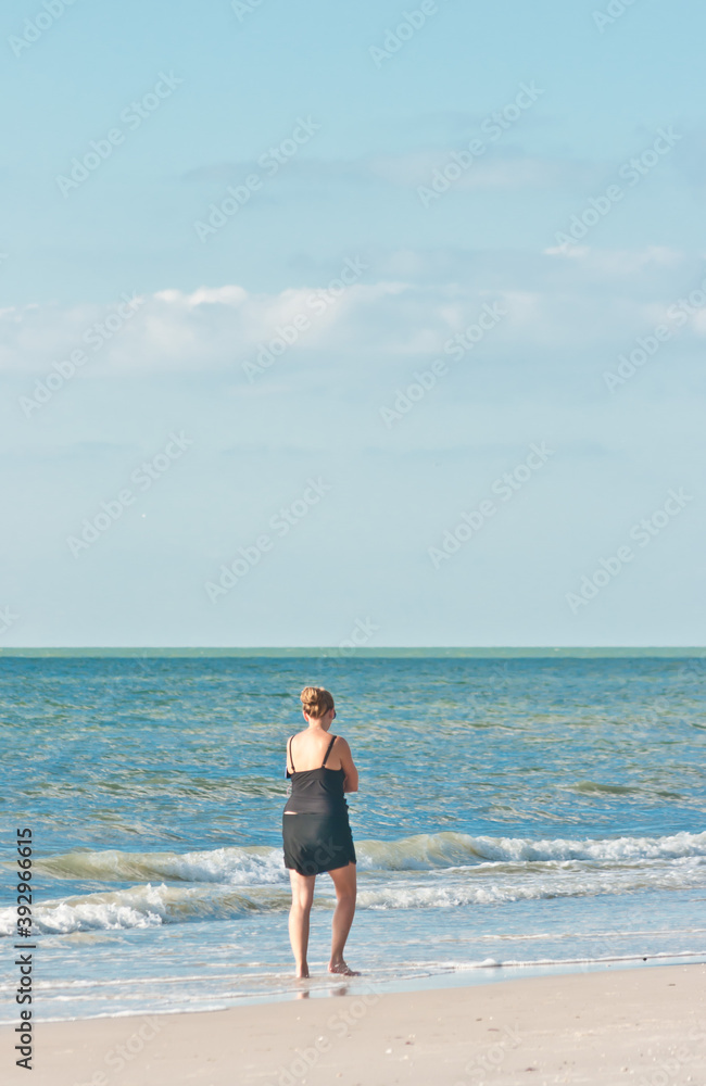 back view, far distance of a middle aged female walking along a tropical, sandy beach on gulf of Mexico. on a sunny morning back view, far distance of a middle aged female walking along a tropical, sandy beach on gulf of Mexico. on a sunny morning
