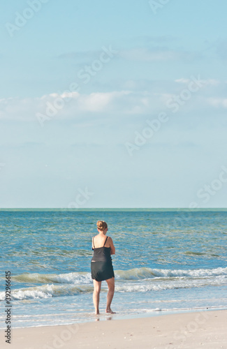 back view, far distance of a middle aged female walking along a tropical, sandy beach on gulf of Mexico. on a sunny morning