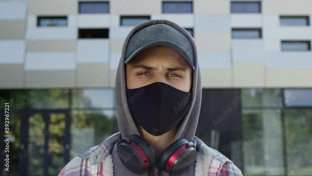 Face Of Young Guy In Black Mask To Protect Against Viruses. He Stands On The Street In Cap And Hood. Face Of Young Guy In Black Mask To Protect Against Viruses. He Stands On The Street In Cap And Hood.
