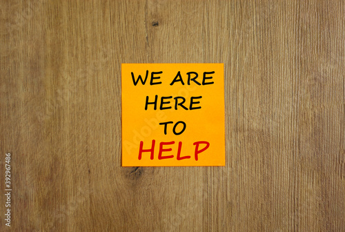 Orange sheet of paper. Text 'we are here to help'. Beautiful wooden background. Business concept, copy space.