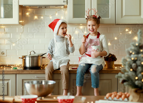 happy children on Christmas eve,   girl and boy eat cookies that they baked together in cozy kitchen at home.