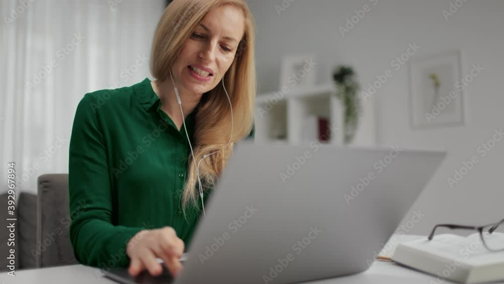 Charming woman in green shirt sitting at home office and talking during video call on wireless laptop. Concept of people and technology. Charming woman in green shirt sitting at home office and talking during video call on wireless laptop. Concept of people and technology.