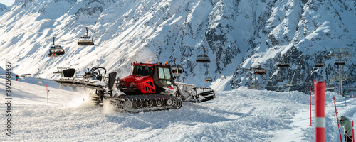 Red modern snowcat ratrack with snowplow snow grooming machine preparing ski slope piste hillalpine skiing winter resort Ischgl in Austria. Heavy machinery mountain equipment track vehicle. panoramic