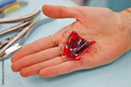 Removable clasp prosthesis in dentist's hand over medical table. Dental prosthesis in hands of doctor close-up. Dentist holds dental bridge. Dentist's office for prosthetics of false teeth. Copy space