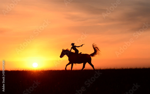 Cowboy riding horse on colorful cloudy sky at sunset with colt 45. Silhouette of cowgirl travel in wild west mountain prairie