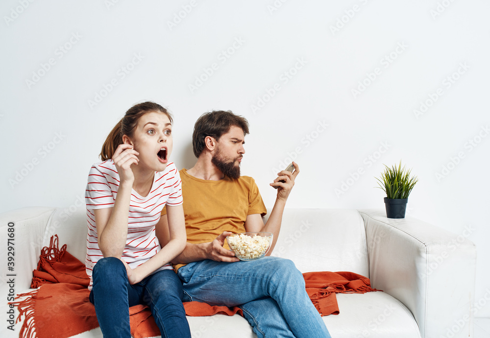 Fun man and energetic woman watching TV on the couch popcorn in a plate family communication Fun man and energetic woman watching TV on the couch popcorn in a plate family communication