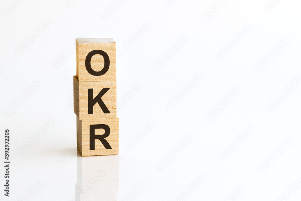 Three wooden cubes with letters OKR - Objectives and Key Results, on white table, more in background, space for text in right down corner Three wooden cubes with letters OKR - Objectives and Key Results, on white table, more in background, space for text in right down corner