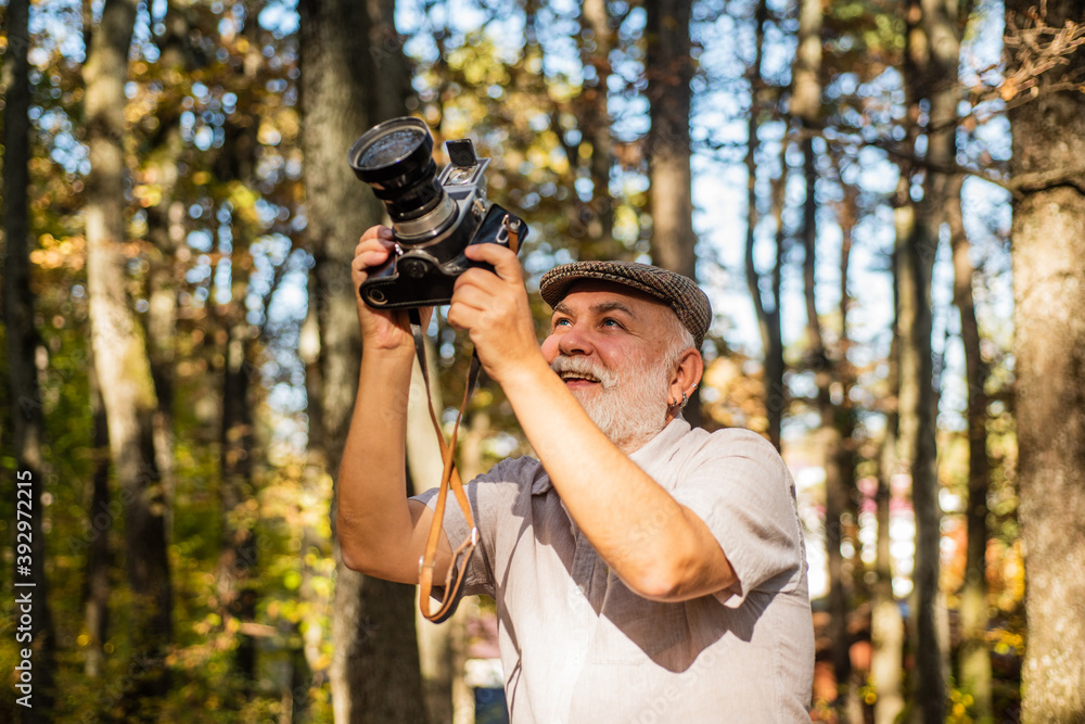 Best camera for professional. Old photographer on autumn day. Pensioner hold vintage camera in forest. Elderly man with photo camera. Using analog camera for shooting. Nature photo shoot session