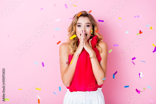 elegant shocked woman in crown under confetti on pink background