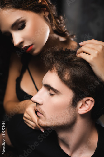Sensual woman with red lips touching chin of young man with closed eyes