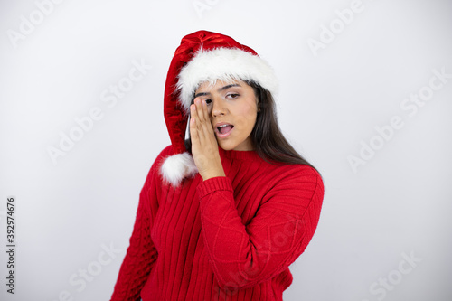 Young beautiful woman wearing a Santa hat over white background hand on mouth telling secret rumor  whispering malicious talk conversation