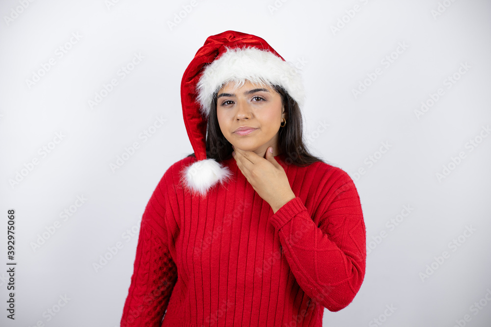 Young beautiful woman wearing a Santa hat over white background touching painful neck, sore throat for flu, clod and infection Young beautiful woman wearing a Santa hat over white background touching painful neck, sore throat for flu, clod and infection