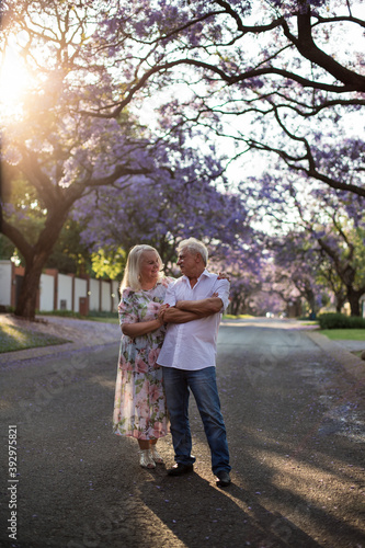 elderly man and woman walk down the street with blooming trees © Olena