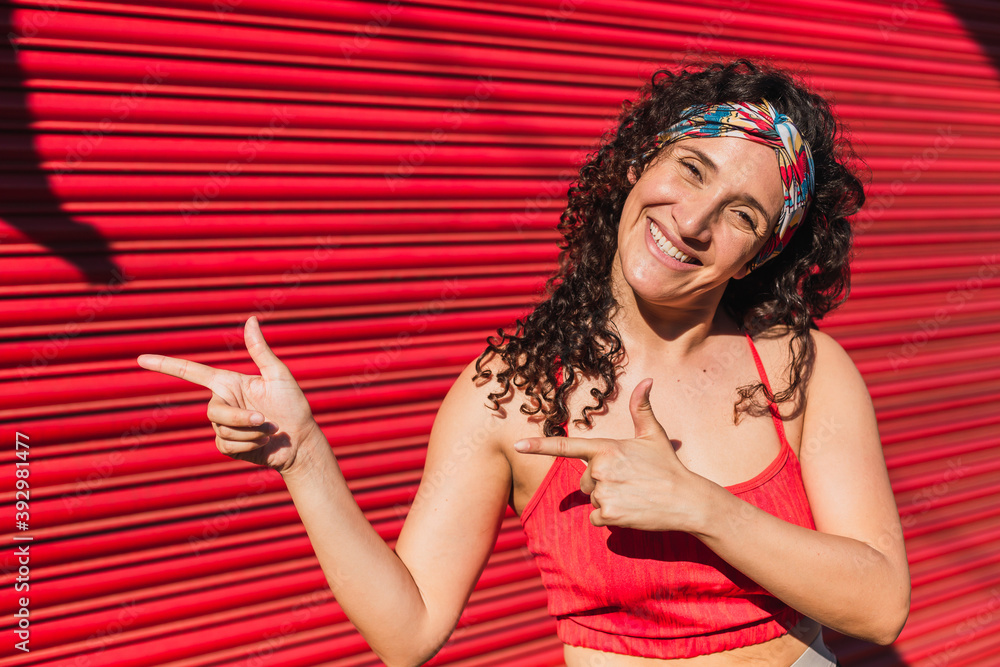 Naklejka premium A young athlete in sportswear pointing her index fingers to the side - Photo of young sportsman positive point index finger isolated empty space on red background .