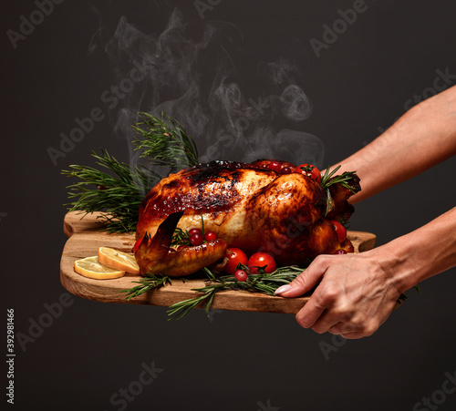 Woman hands hold plate with cooked thanksgiving turkey or chicken for christmas dinner evening with steam smoke on wooden rustic plate garnished with cherry berries and fruits on dark background