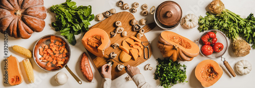 Fall, winter vegan cooking ingredients layout. Flat-lay of female hands cutting mushrooms over white plain table with pumpkins, celery, corn, sweet potato, top view. Vegan, vegetarian, clean eating