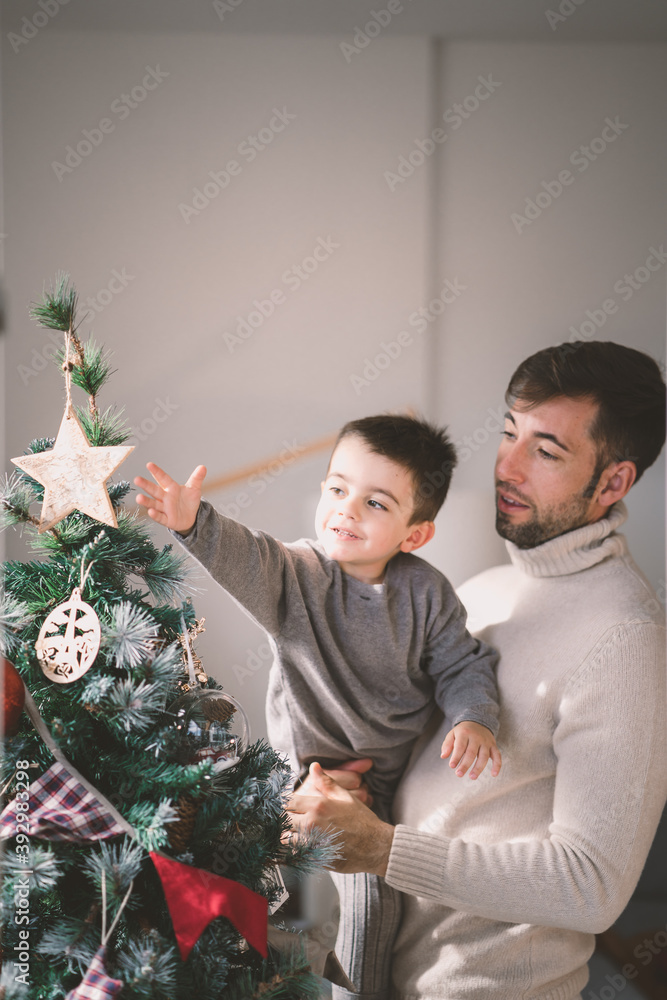 Young father helping his little son to place a decor figure on the christmas tree at home Young father helping his little son to place a decor figure on the christmas tree at home