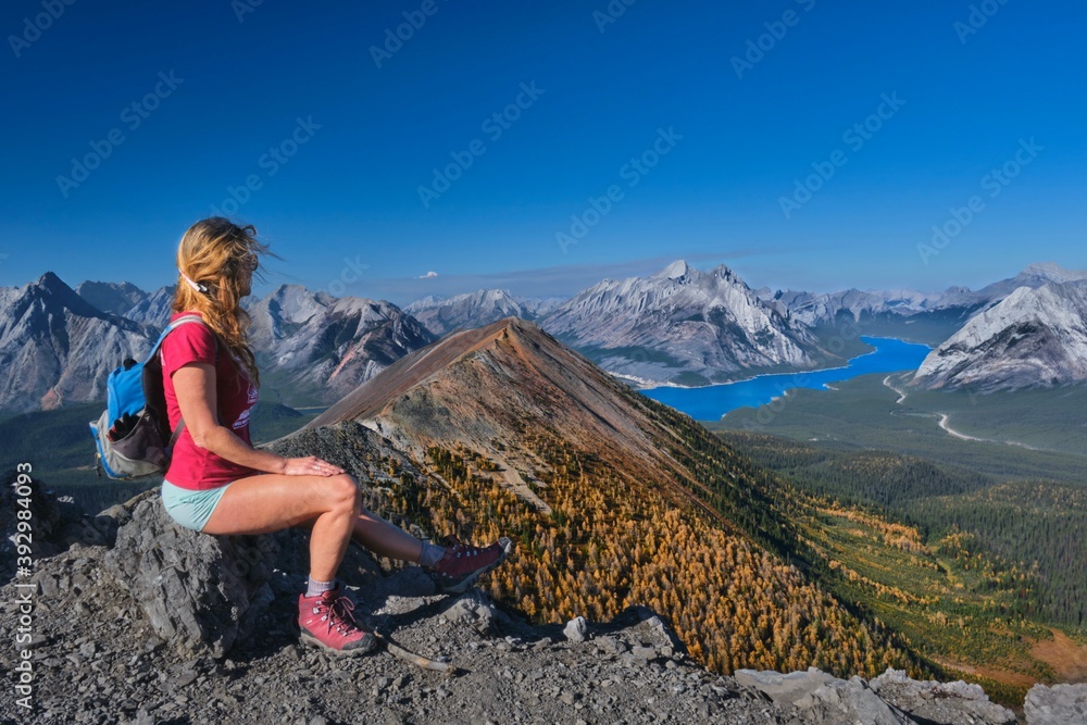 Naklejka premium Middle age caucasian woman hiker on mountain top relaxing and enjoying view of lake and mountains in Canadian Rockies. Alberta. Canada