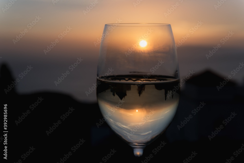 a glass of white wine where the sunset is reflected