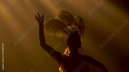 Silhouette of a sexy young woman in a Brazilian samba carnival costume with yellow plumage of feathers dances against a background of blue lights. Close up in slow motion. photo
